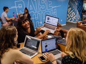Students smiling and using their laptops in a common space